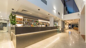 Zona de bar moderna con una barra larga, estantes llenos de botellas de licores y un amplio ventanal.