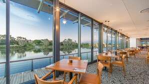 Un restaurante con amplios ventanales con vistas a un lago, mesas y sillas de madera, y un suelo con diseño.