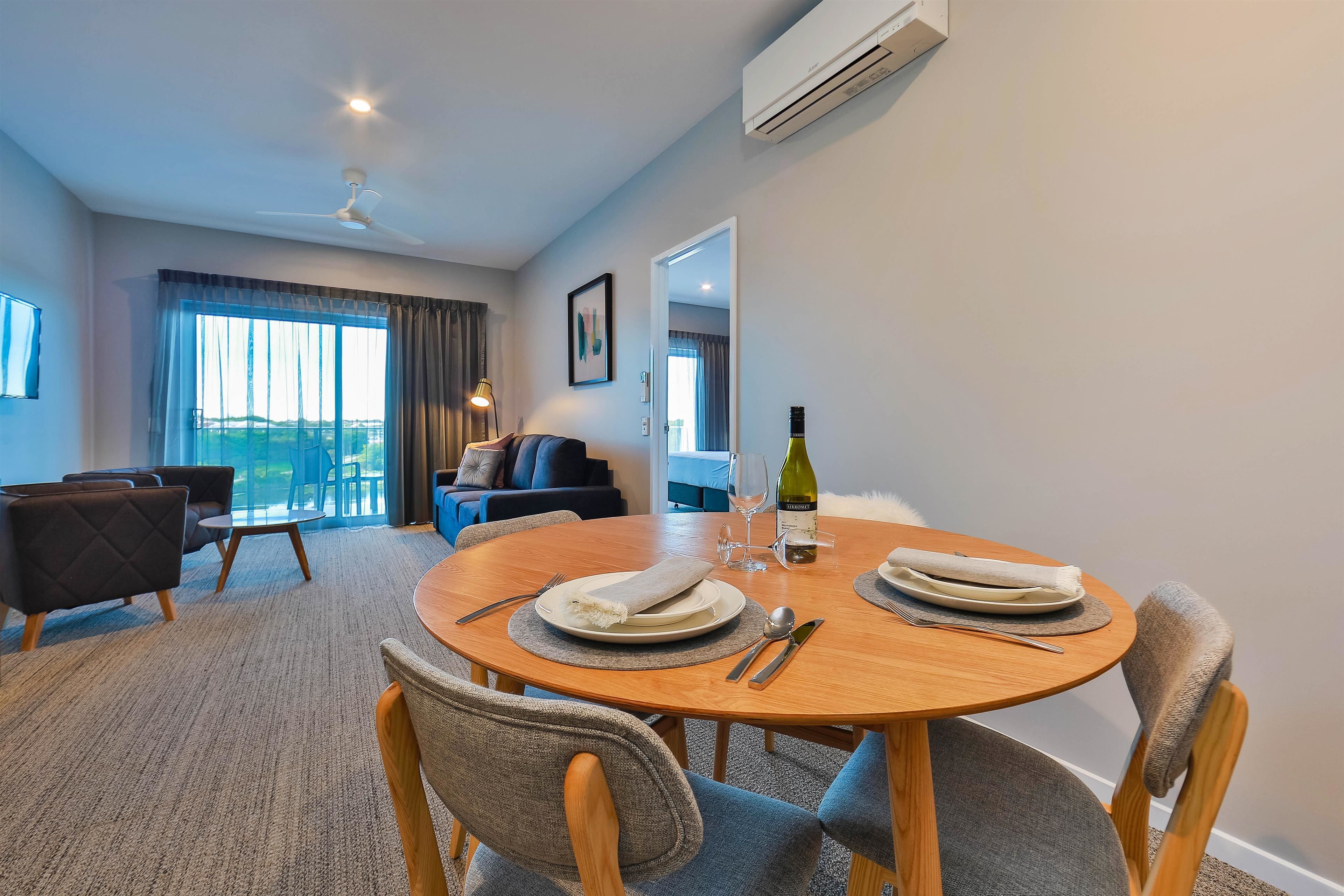 A dining area with a round wooden table set for two, a sofa, and a view of the outdoors.