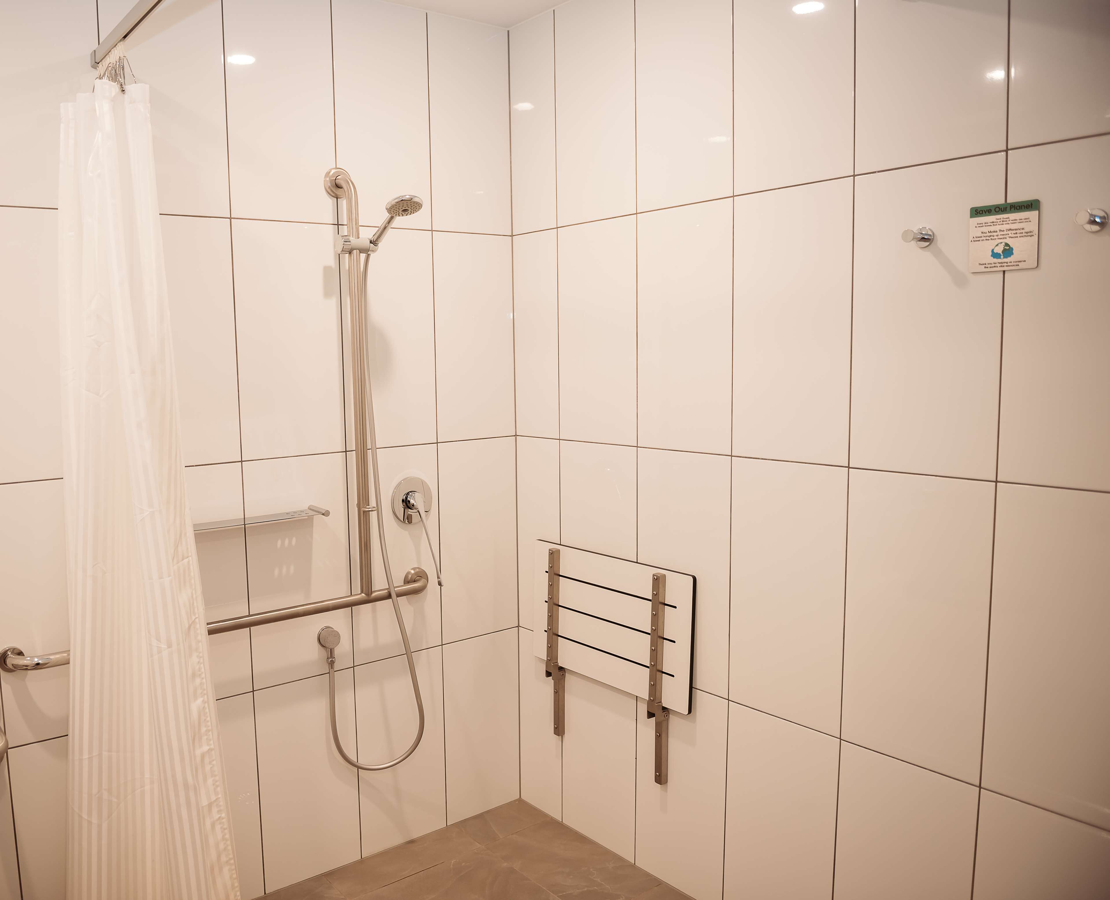 A shower area with white tiled walls, a showerhead, a handheld shower, and a towel rack.