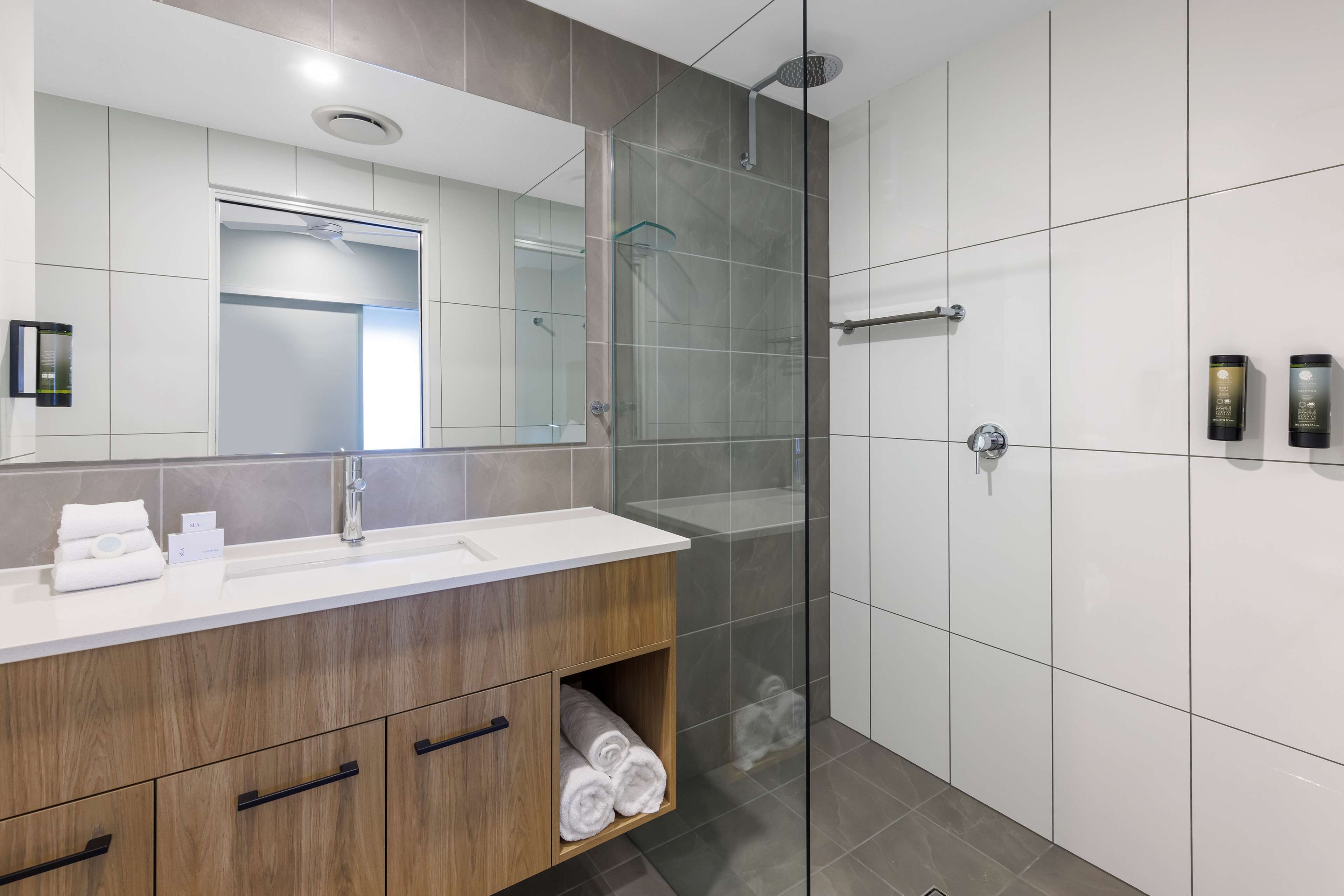 Une salle de bain moderne avec une douche à parois de verre, un meuble-lavabo en bois et un grand miroir.