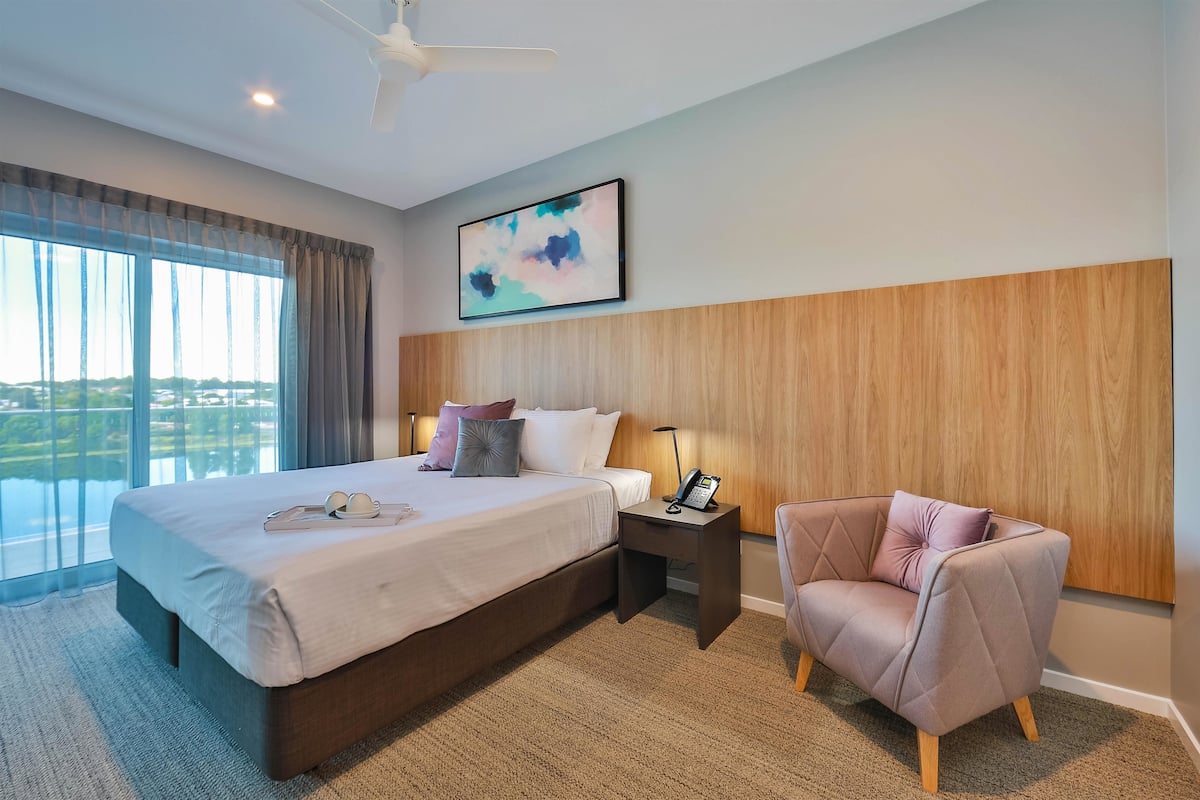 Une chambre d’hôtel avec un grand lit, une chaise, une table de chevet avec un téléphone et une vue sur l’extérieur.