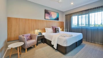 A hotel room with a bed, a chair, a small table, a ceiling fan, and a window with curtains.