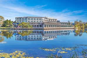 Un bâtiment moderne à la façade vitrée, qui se reflète dans l’eau, et un quai agrémenté de parasols.