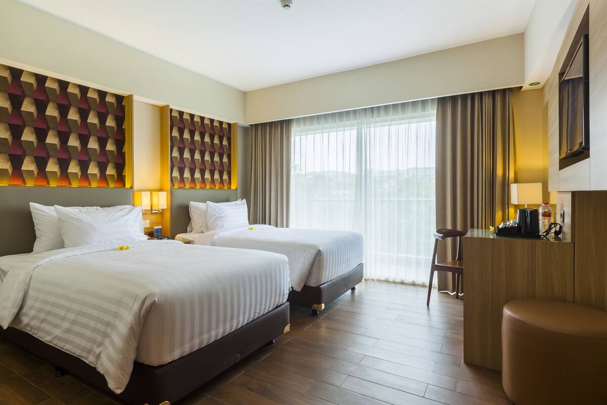 Habitació d'hotel amb dos llits, una taula de treball i un gran finestral amb cortines.
