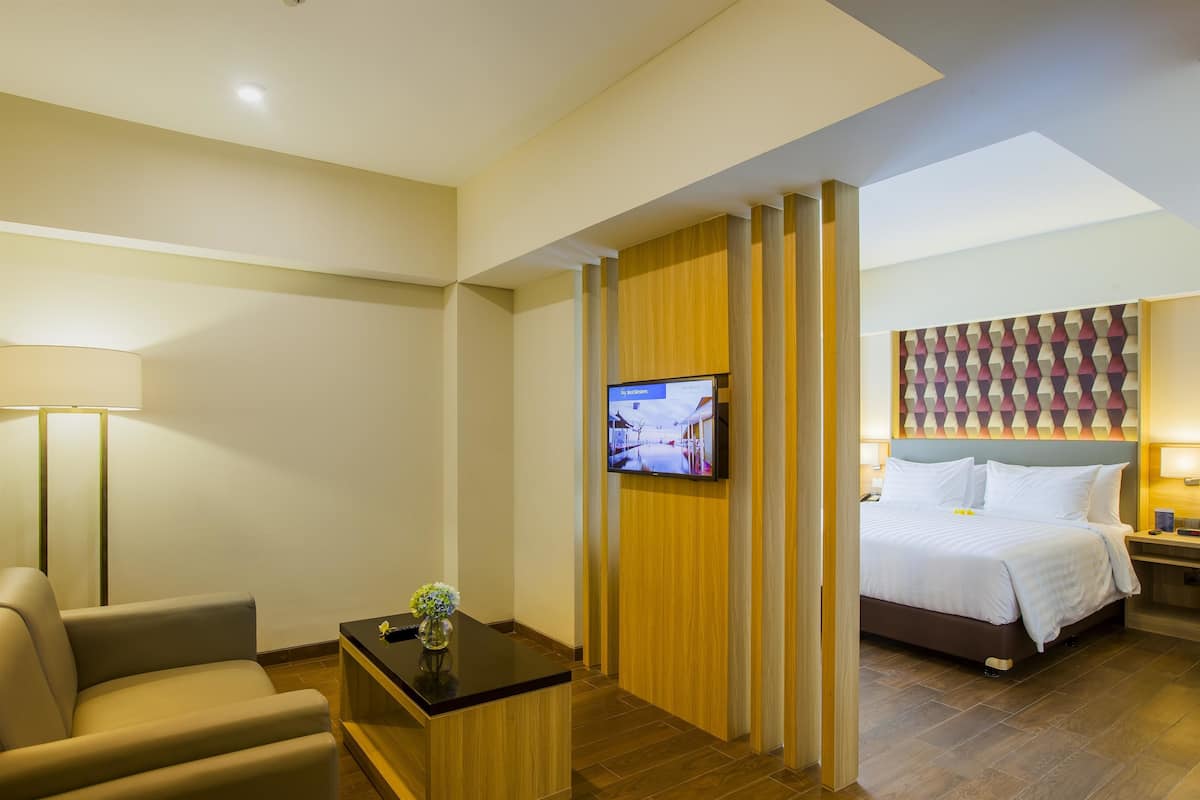 Habitació d'hotel amb llit, televisió penjada a la paret, escriptori amb un ram de flors i sofà.