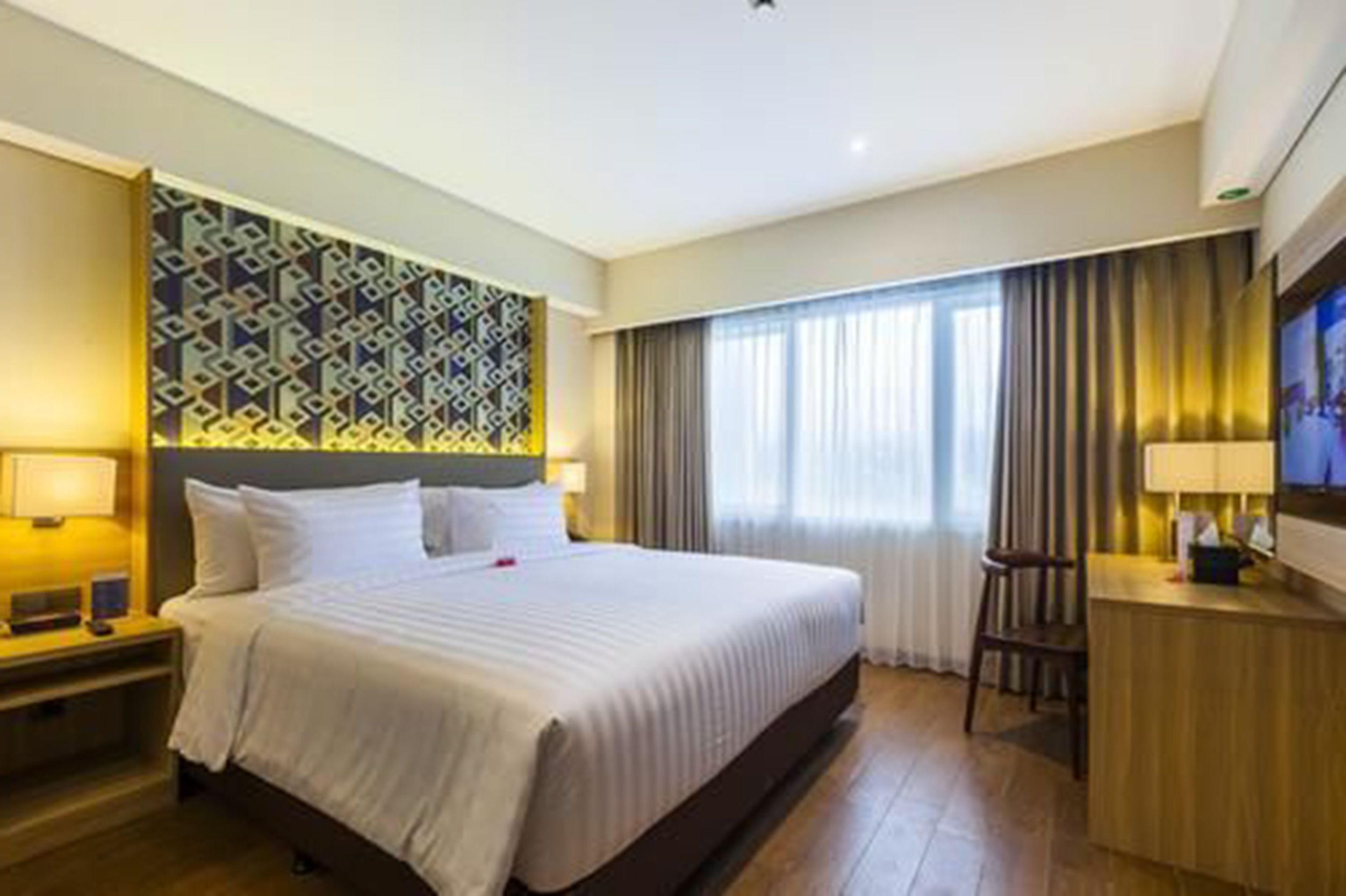 Een hotelkamer met een groot bed, een bureau met stoel, een televisie en een behangen muur.