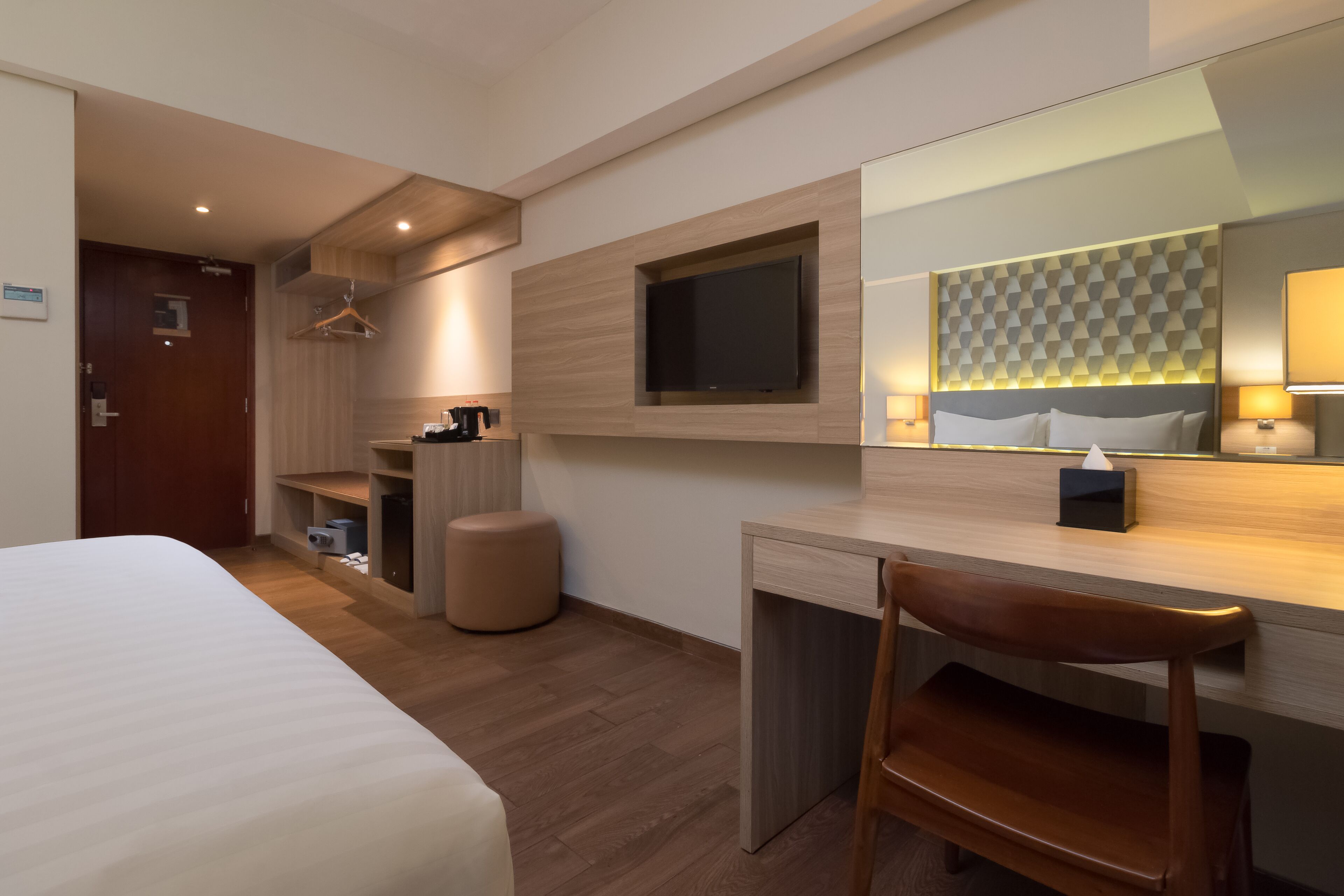 Una habitación de hotel moderna con una cama grande, un escritorio con silla, un televisor montado en la pared y un armario.