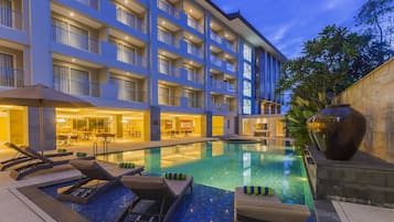 A hotel with a swimming pool, lounge chairs, and a large decorative vase.