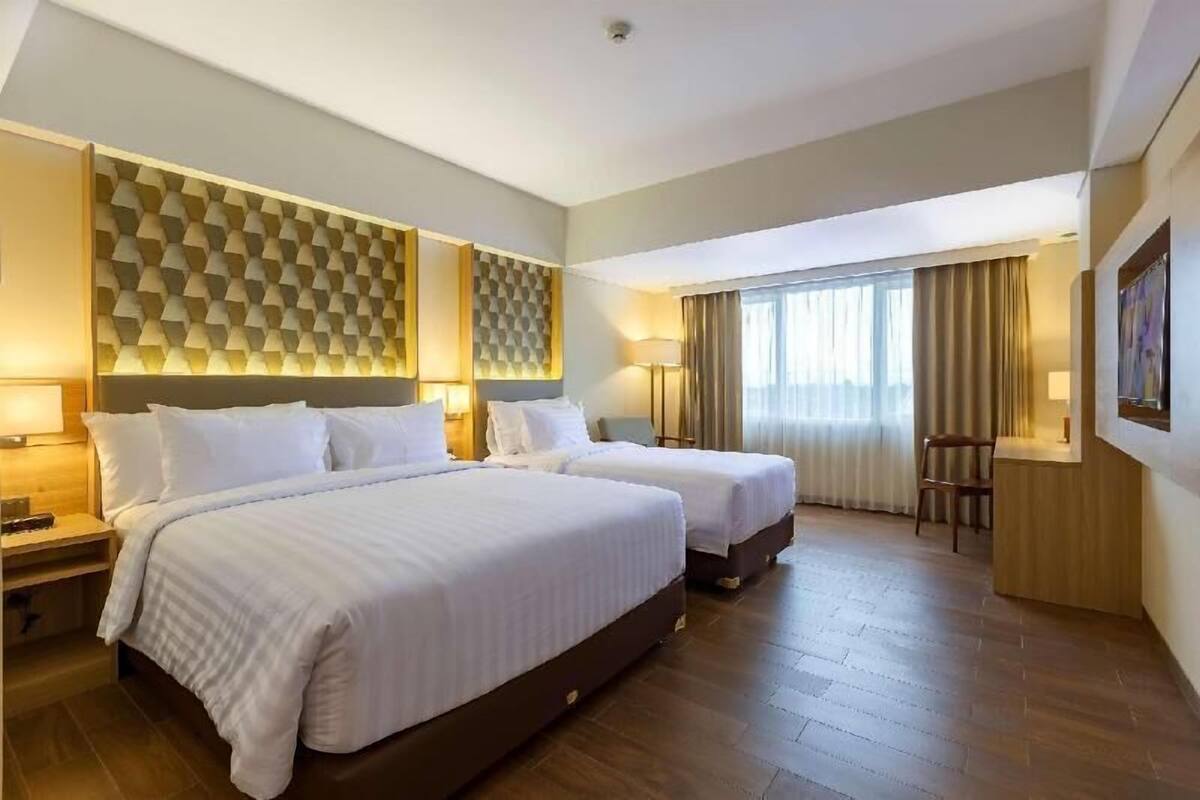 Habitació d'hotel amb dos llits, un escriptori, una cadira, una finestra gran amb cortines i una paret amb un disseny.