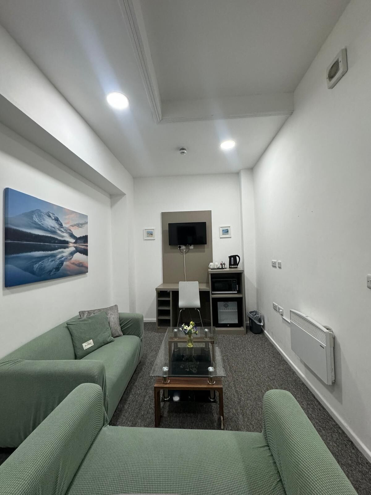 Ein modernes Wohnzimmer mit einem grünen Sofa, einem Couchtisch, einem Flachbildfernseher und einem Gemälde von einer Berglandschaft.