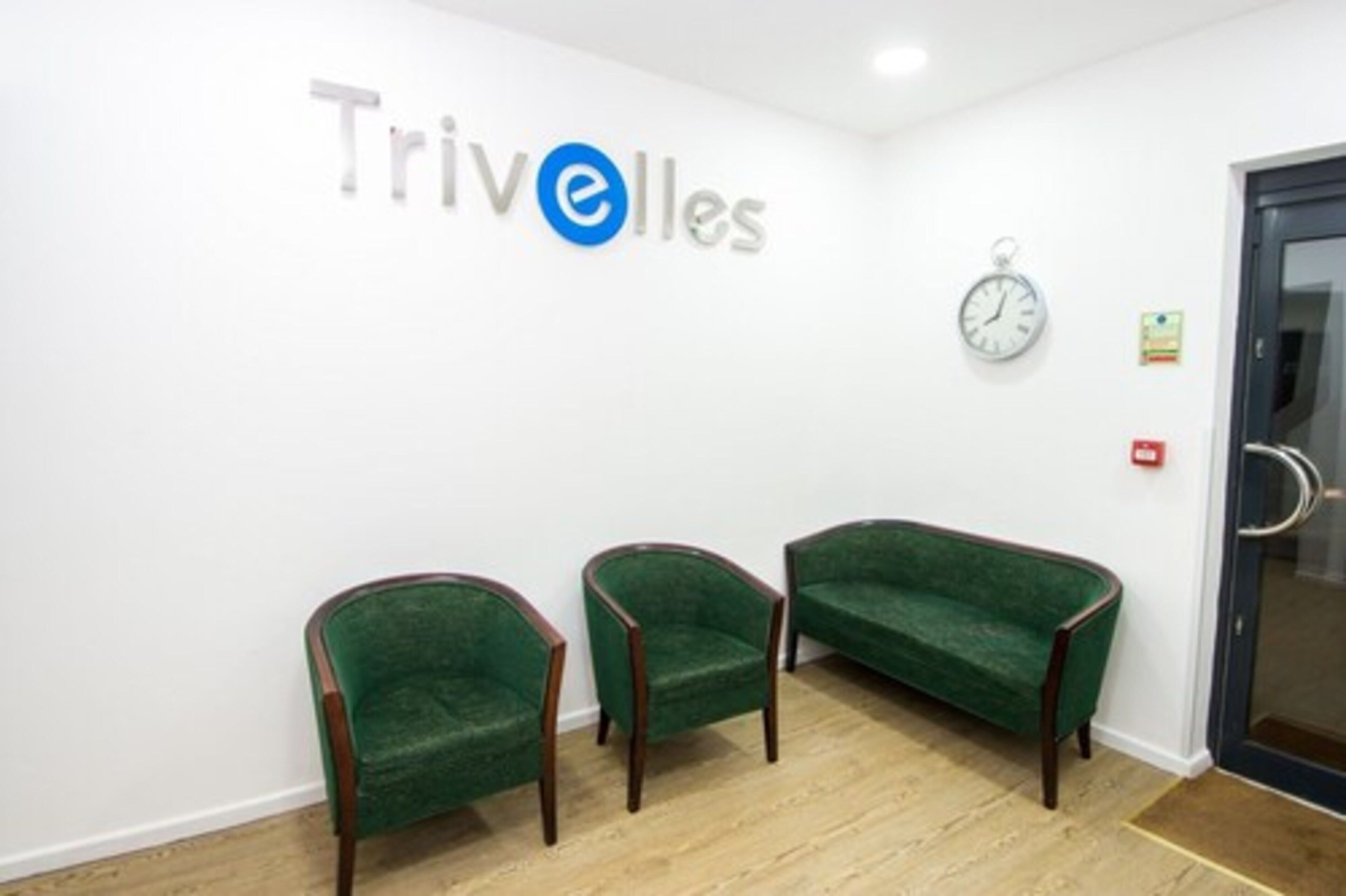 Une salle d’attente avec le logo de Trivelles sur le mur, trois chaises vertes, une horloge et une porte.