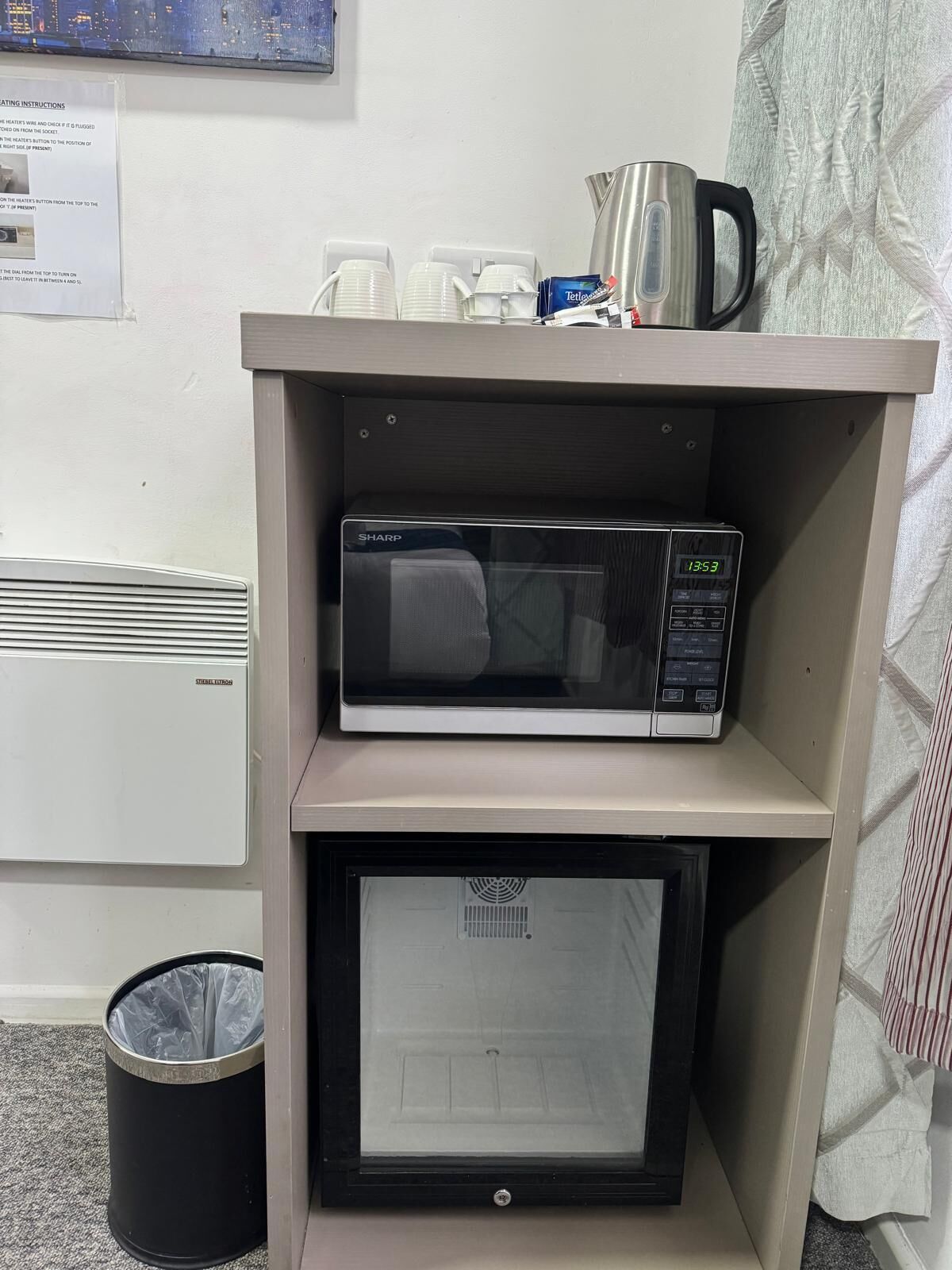 Un microondas sobre una repisa, con una tetera y tazas encima.