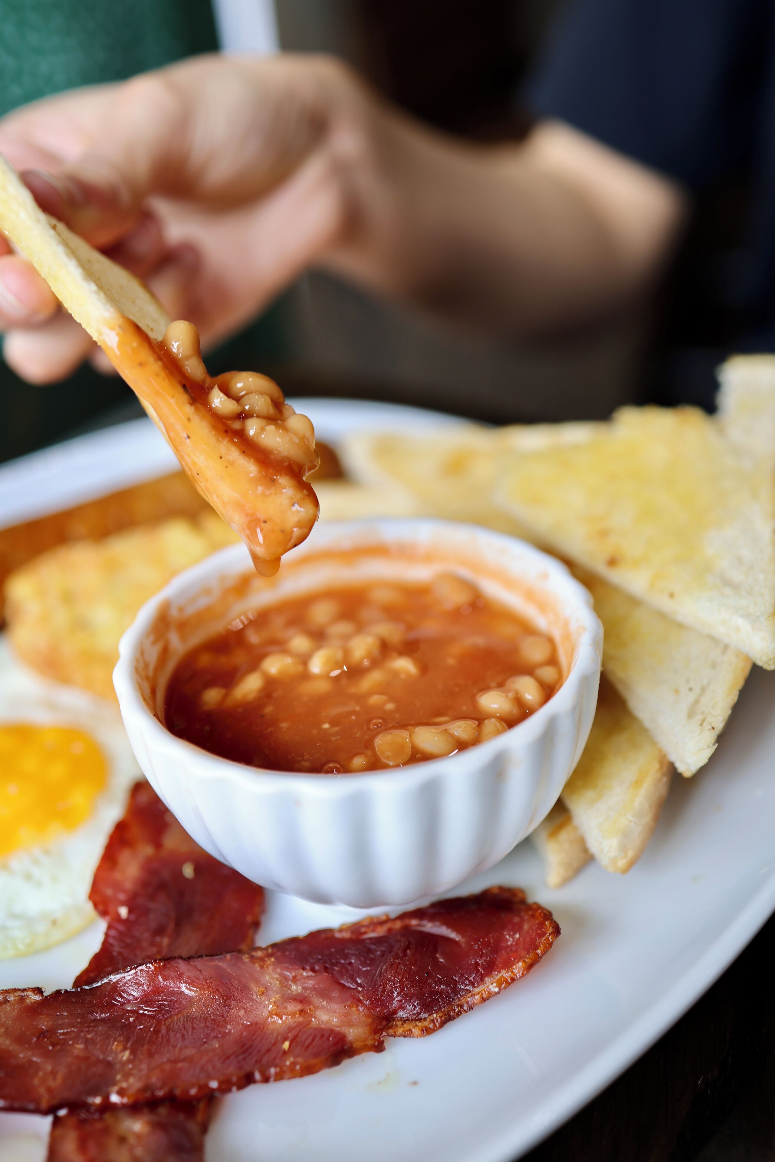 A plate with beans, toast, bacon, and an egg.