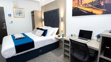 Ein Hotelzimmer mit Bett, Schreibtisch mit Laptop, Stuhl und Stadtbild an der Wand.