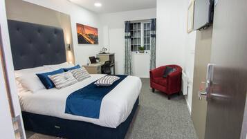 Habitación de hotel con una cama grande, un escritorio, una silla, un televisor y una ventana con cortinas.