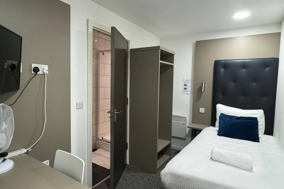 Ein Hotelzimmer mit Bett, Nachttisch und Schreibtisch mit Stuhl. Es gibt einen Kleiderschrank und einen Spiegel an der Wand.