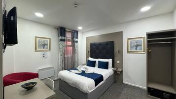 A hotel room with a bed, a desk, a chair, a wardrobe, and a television.