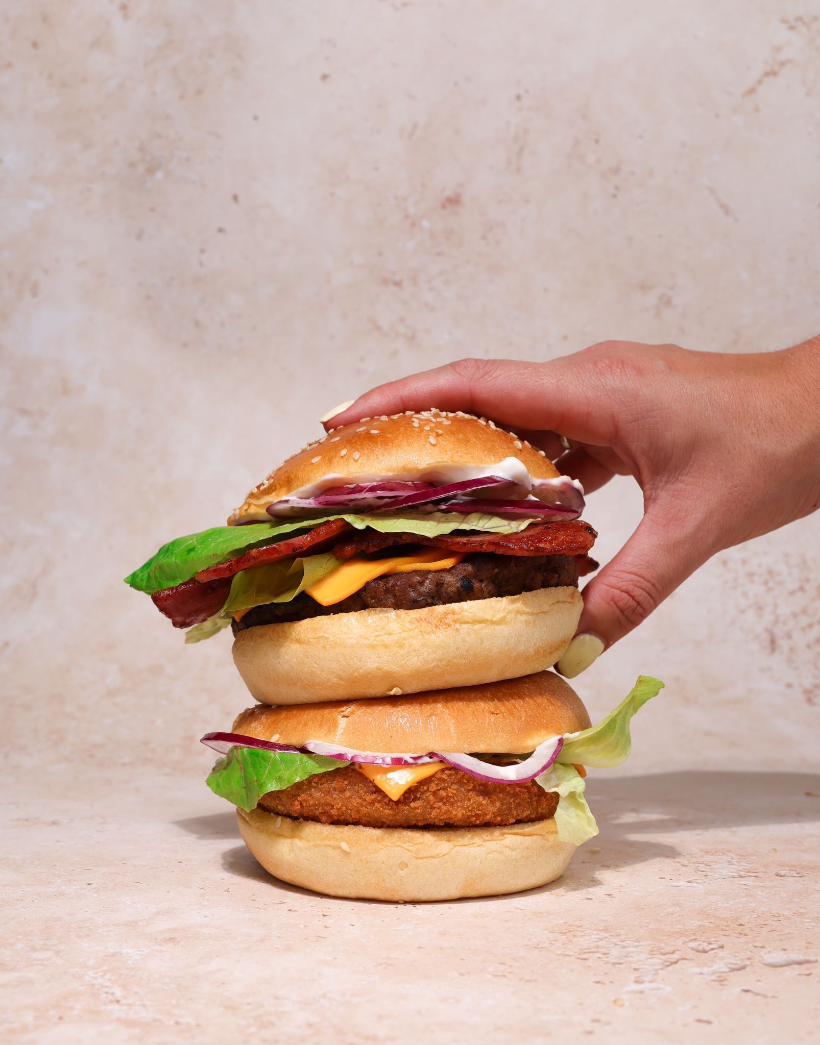 Een hand houdt een burger met meerdere lagen vast, met zichtbare ingrediënten zoals sla, kaas en een runderburger.