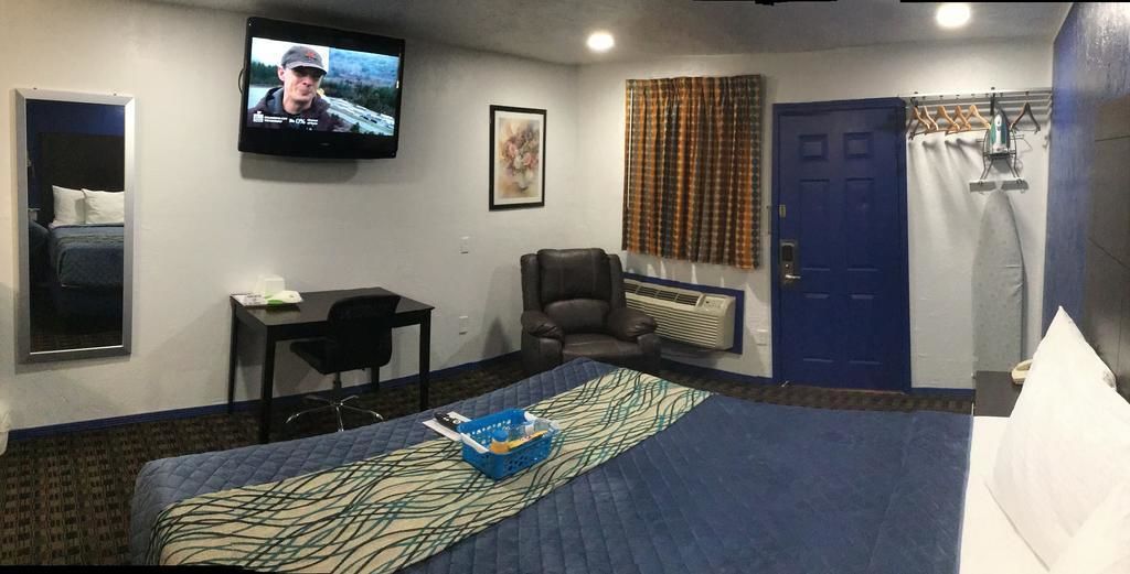 A hotel room with a bed, a desk, a chair, a television, a framed picture, a window with curtains, and a door.