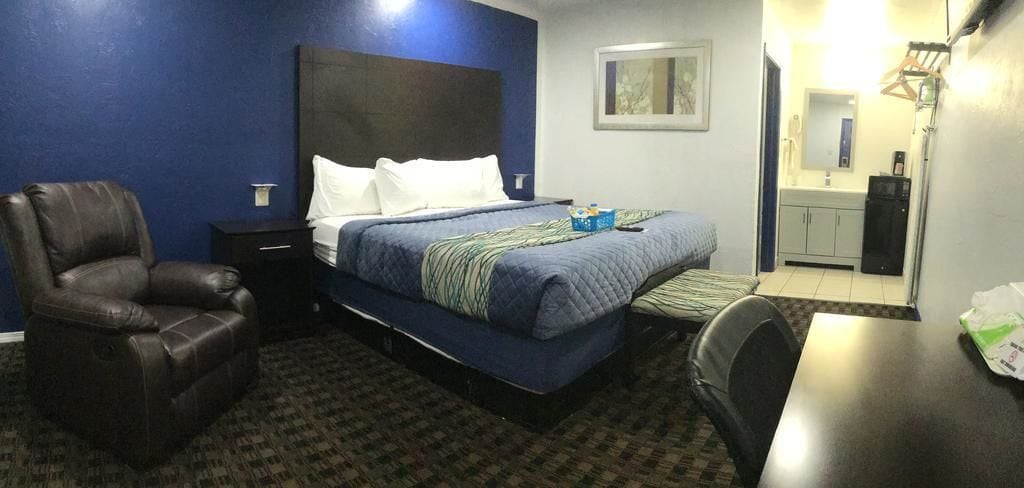 A hotel room with a bed, a chair, a desk, and a small kitchenette.