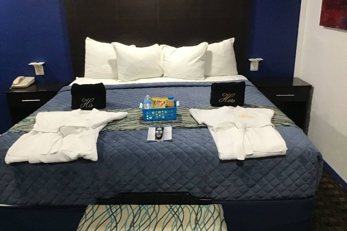 A hotel room with a bed, two nightstands, a phone, a basket of toiletries, and two robes.
