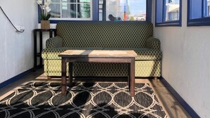 Une pièce avec un tapis à motifs, un canapé vert, une table en bois et une grande fenêtre ornée de bordures bleues.