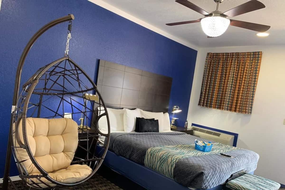 A bedroom with a bed, a hanging chair, a ceiling fan, and a window with curtains.