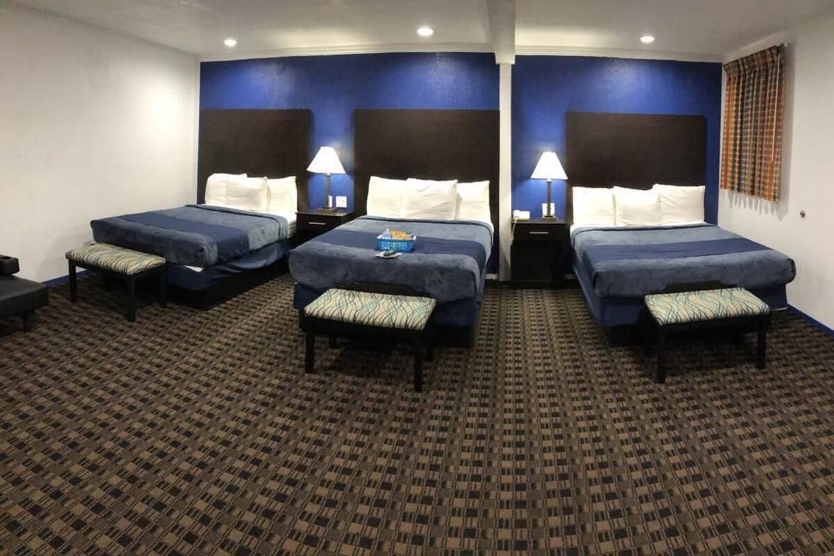 A hotel room with two beds, each with a pillow and a lamp, and a bench between them.