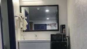 Une petite salle de bain avec un meuble-lavabo blanc, un miroir, un four à micro-ondes et un sèche-cheveux.