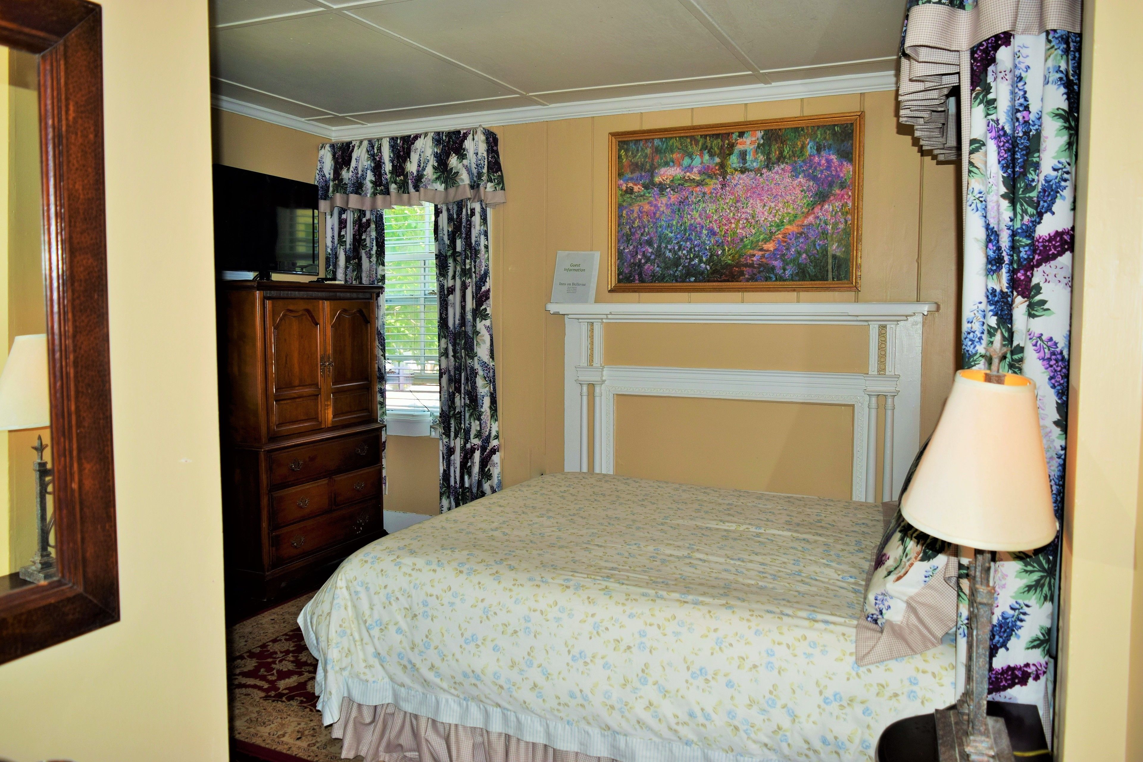 A bedroom with a bed, a dresser, a painting, and a fireplace.