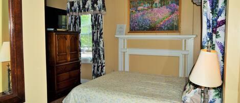 A bedroom with a bed, a dresser, a painting, and a fireplace.