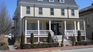 A two-story hotel with a front porch, a sign reading "Hotel," and a staircase leading to the entrance. - Bellevue Manor (Newport)