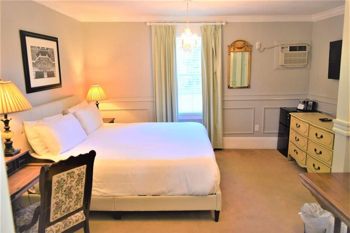 A neatly arranged bedroom with a bed, bedside lamps, a dresser, a chair, and a mirror.
