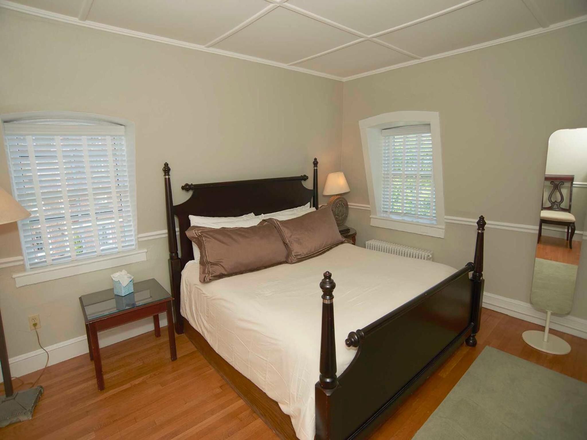 A bedroom with a four-poster bed, two bedside tables, a nightstand, and a mirror.
