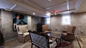 A room with a stone wall, a poster, a sofa, two armchairs, a glass table, and a patterned rug. - Bellevue Manor (Newport)