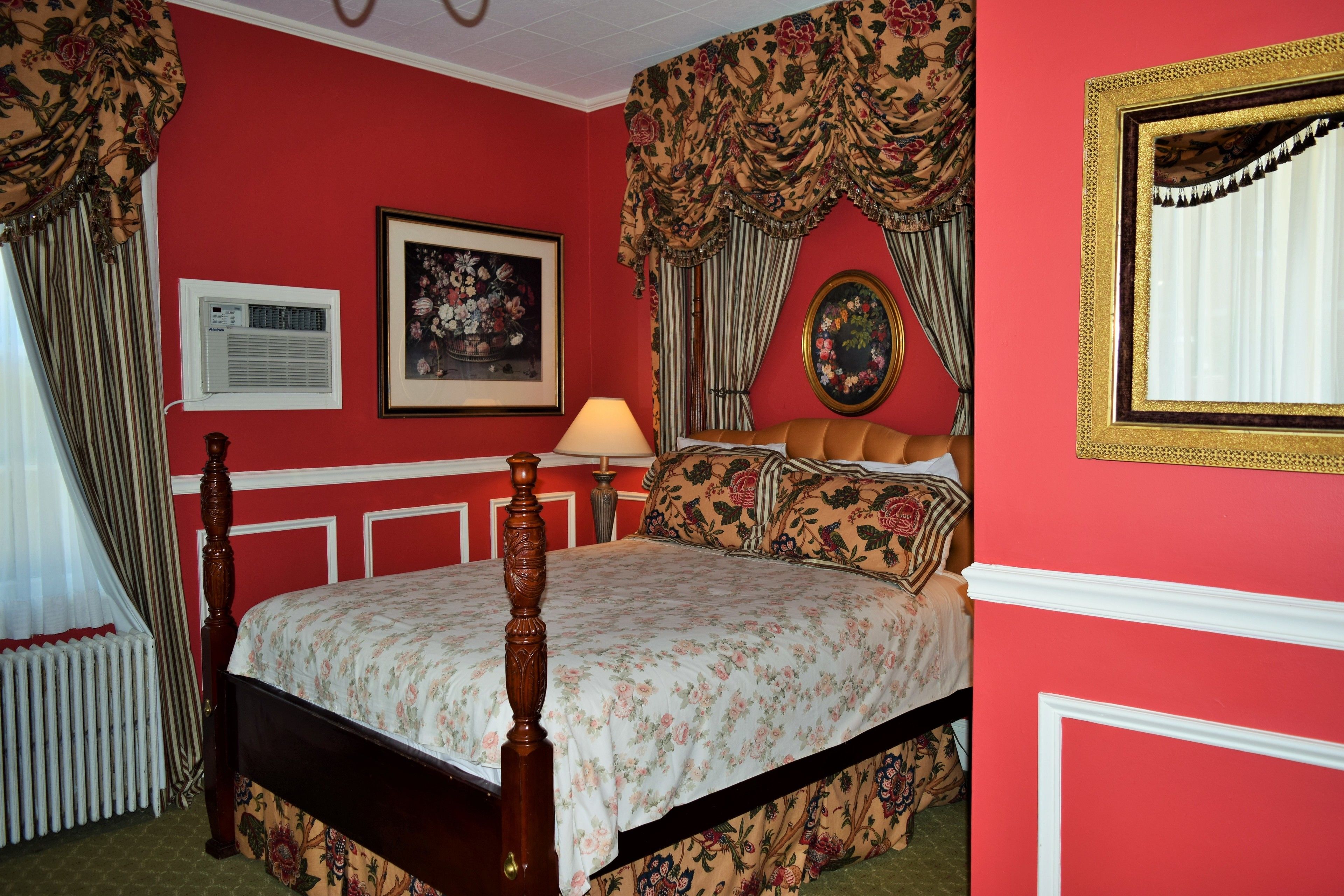 A bedroom with a four-poster bed, floral wallpaper, and a red wall.