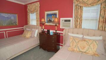A hotel room with two single beds, a wooden dresser, a painting, a lamp, and an air conditioning unit.