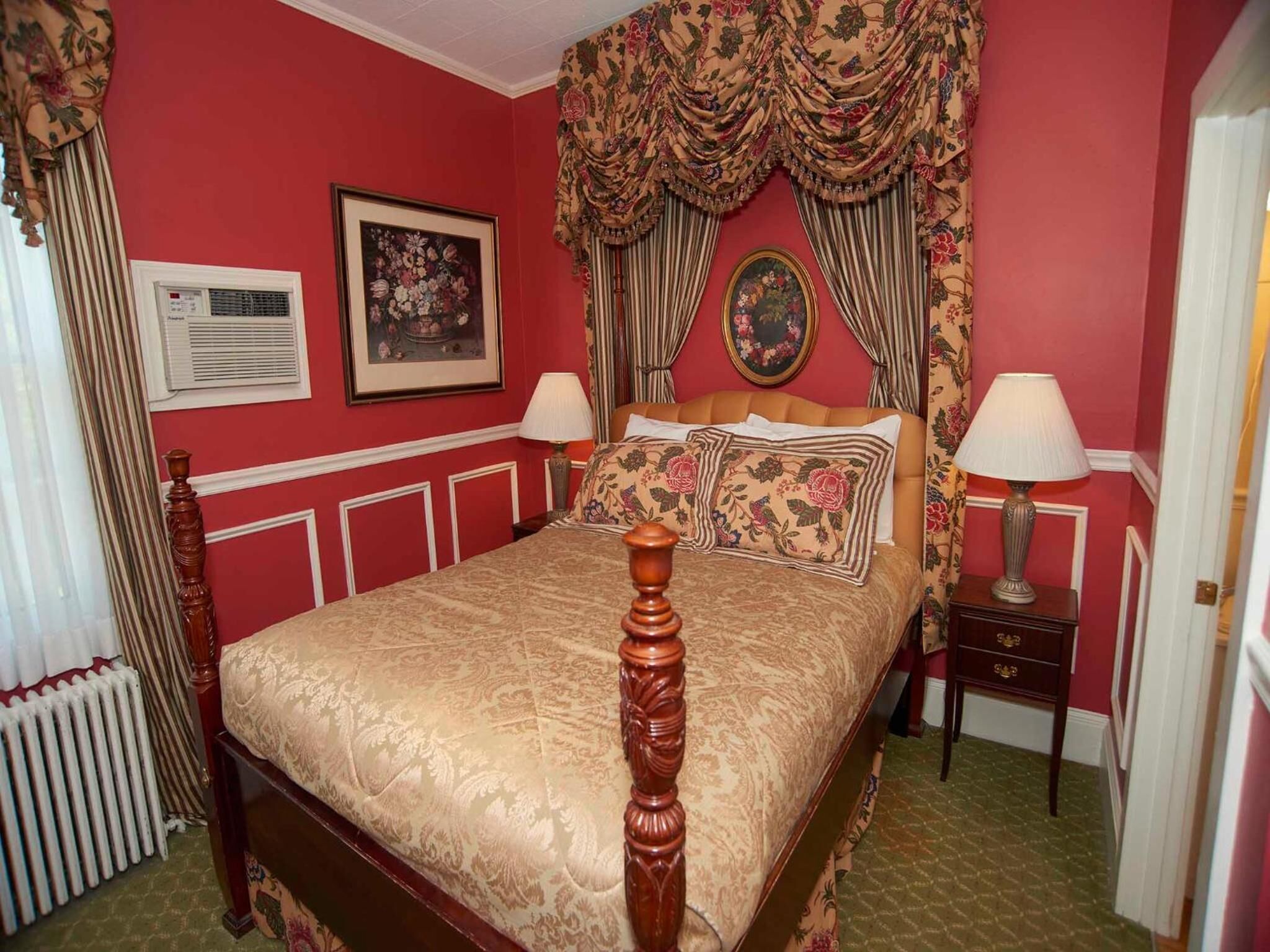 A traditional bedroom with a four-poster bed, floral curtains, and a radiator.