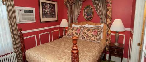 A traditional bedroom with a four-poster bed, floral curtains, and a radiator.