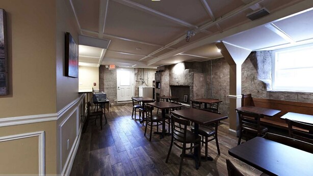 A restaurant interior with wooden tables and chairs, stone walls, and a high ceiling with exposed beams. - Bellevue Manor (Newport)