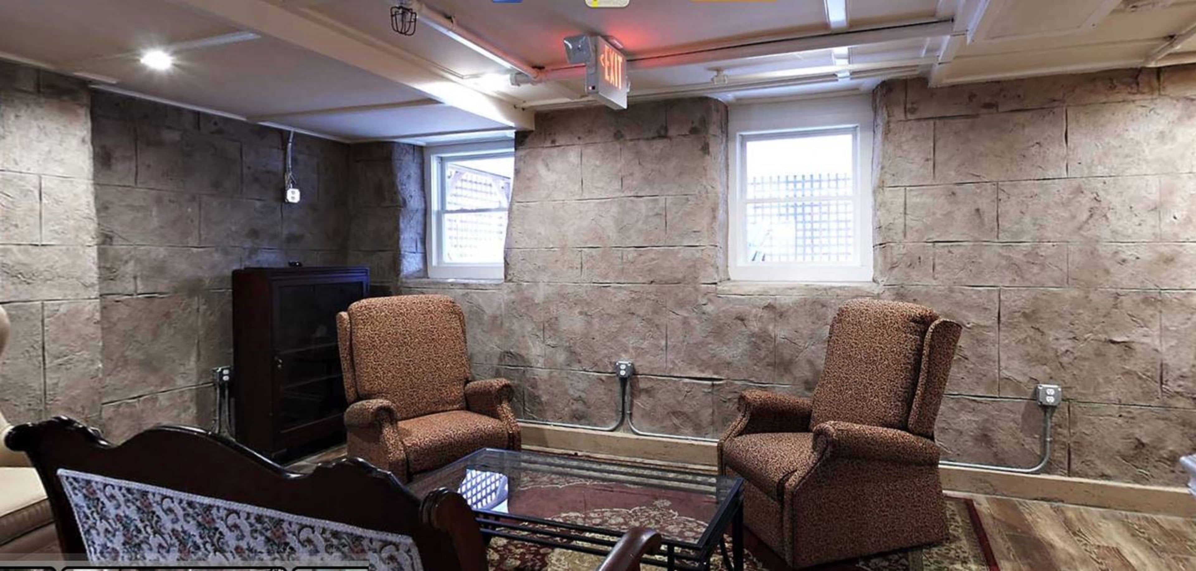 A room with stone walls, two armchairs, a glass coffee table, and a patterned sofa.