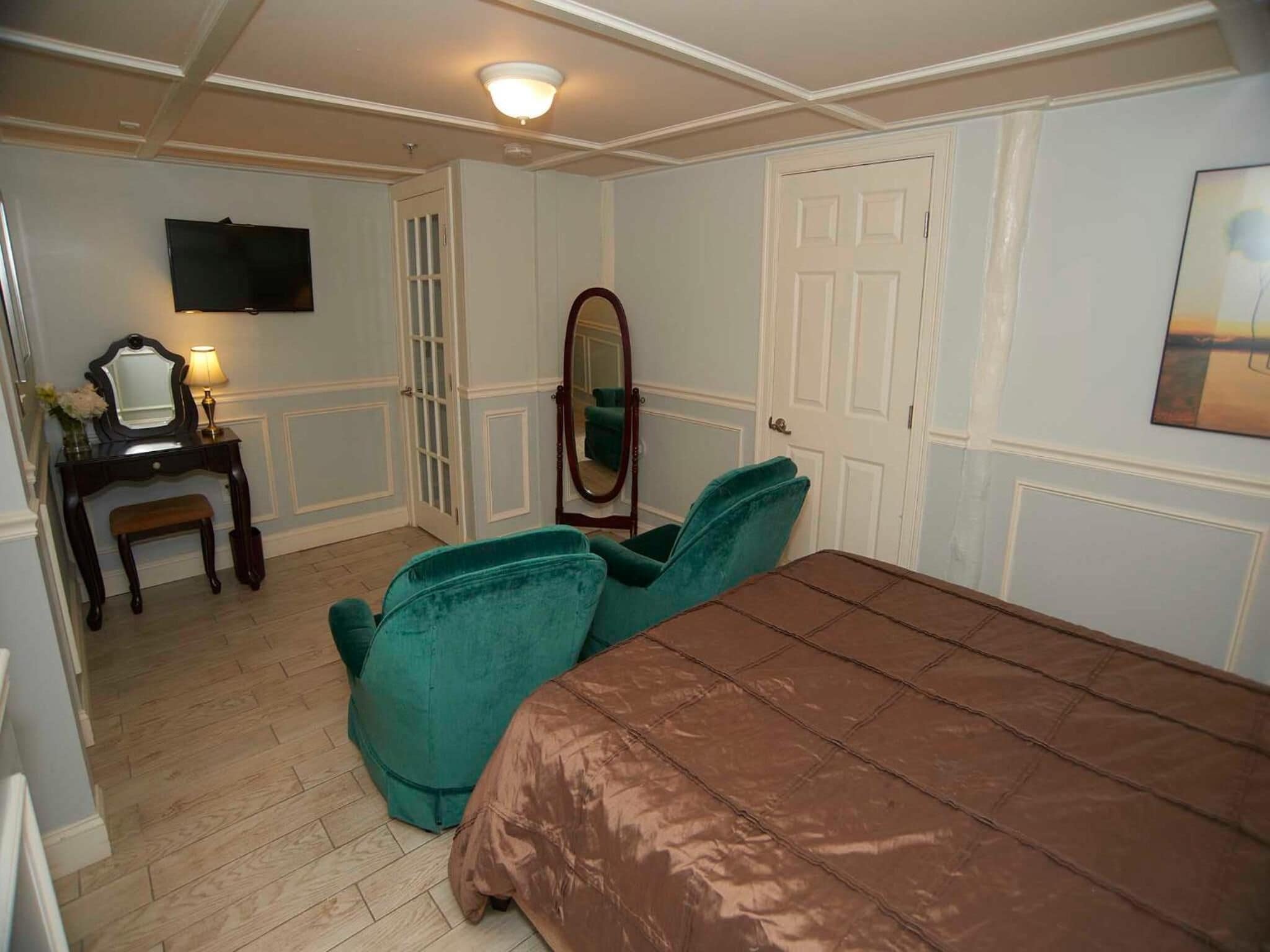 Un dormitorio con una cama, un tocador con espejo, una televisión y una puerta.