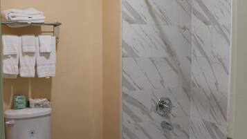 A bathroom with a toilet, a shower with a glass door, and a towel rack with folded towels.