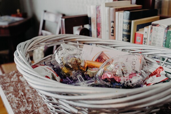 A wicker basket filled with various items, including books and wrapped objects, placed on a table with a patterned rug. - Aurora Staples Inn (Stillwater)