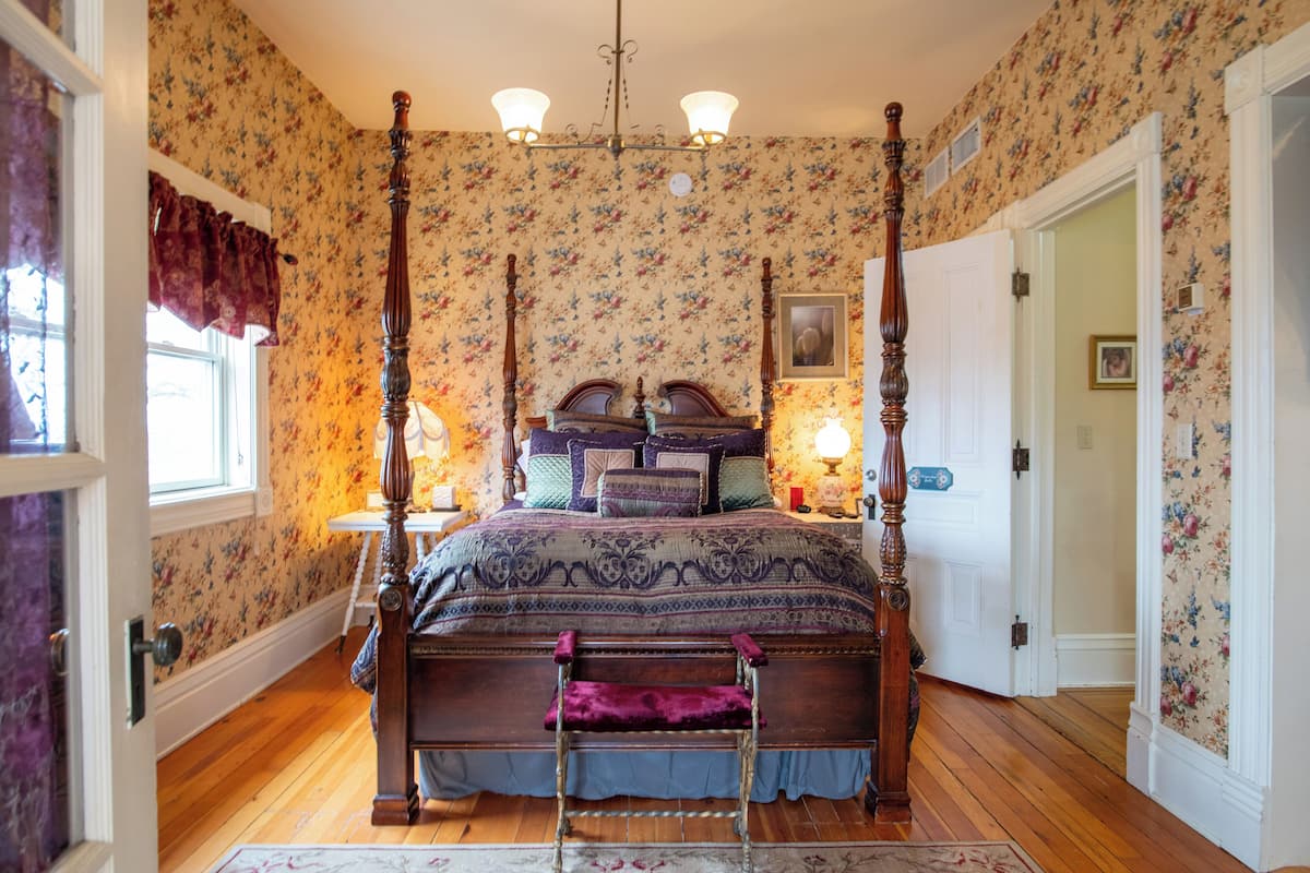Un lit à baldaquin avec un cadre en bois, une chambre décorée de papier peint à motifs floraux et un plancher en bois.