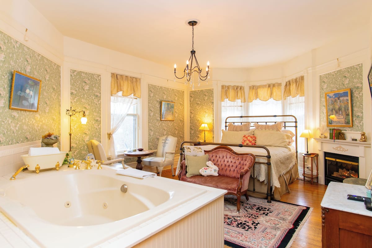 Une chambre à coucher classique avec une grande baignoire, un fauteuil ancien et une cheminée.