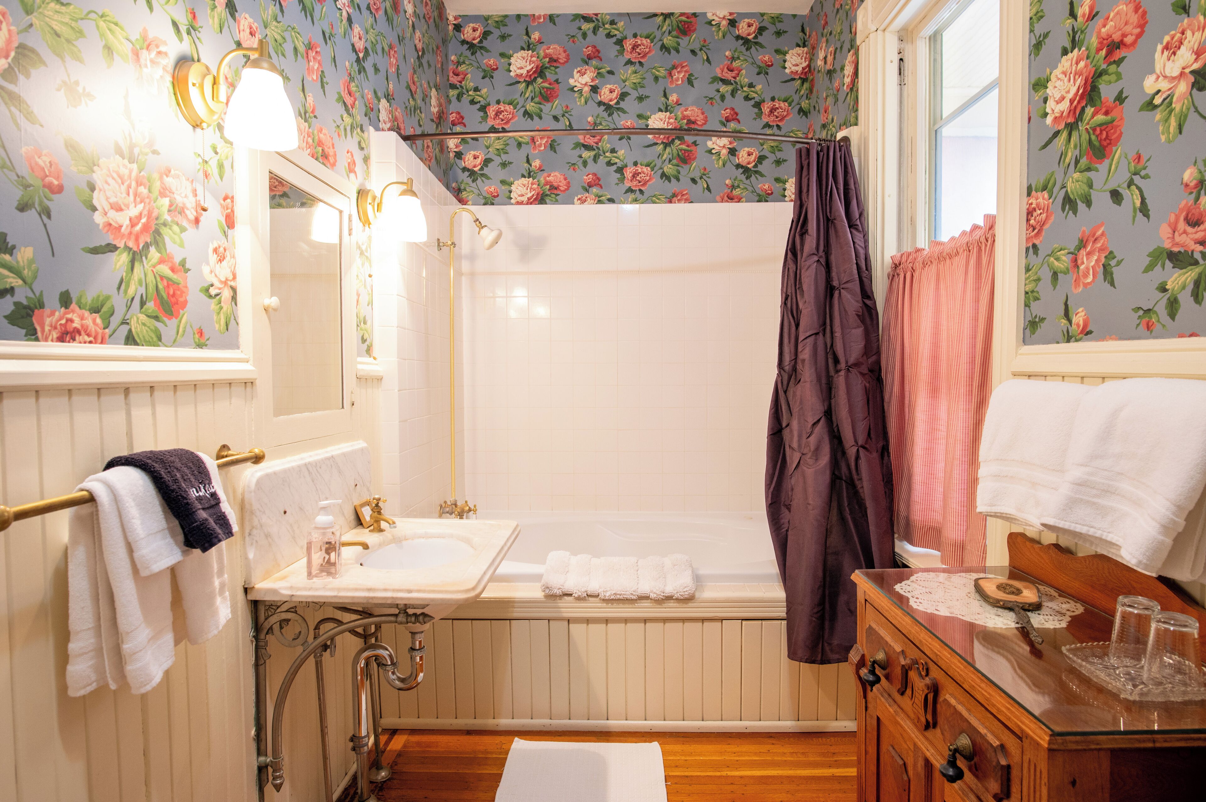 A bathroom with a wooden vanity, a bathtub, a shower curtain, and floral wallpaper.
