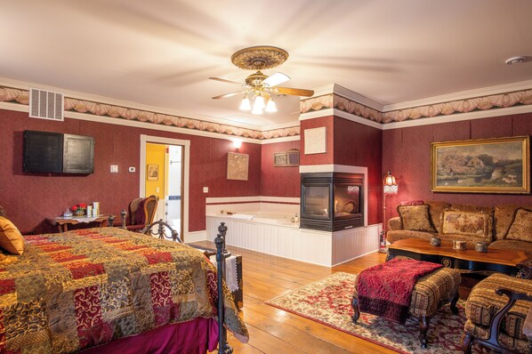 A room with a bed, a sofa, a fireplace, a ceiling fan, and a painting on the wall. - Aurora Staples Inn (Stillwater)