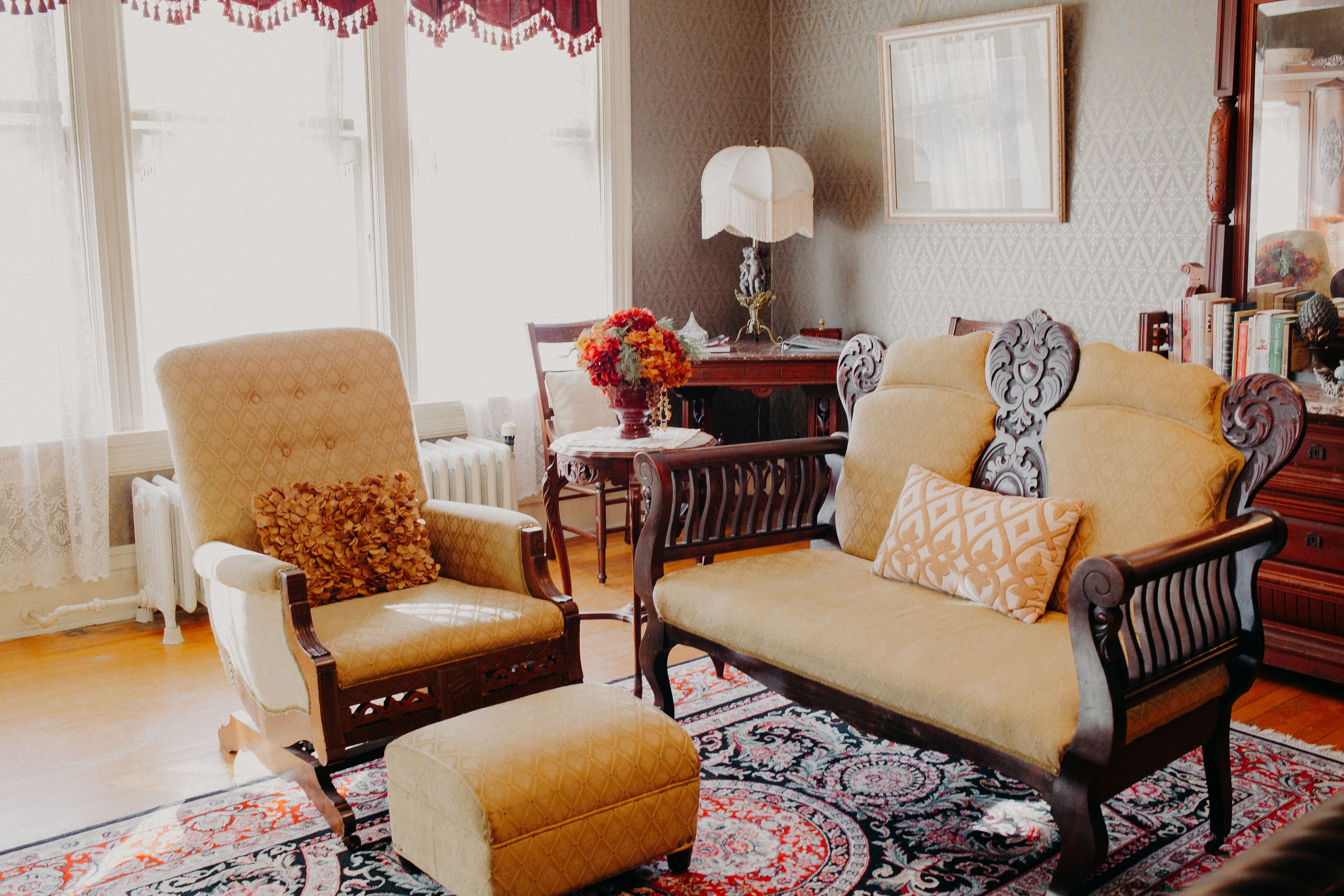 Una sala de estar con sofá, sillón y reposapiés, una mesa con lámpara, y una estantería.